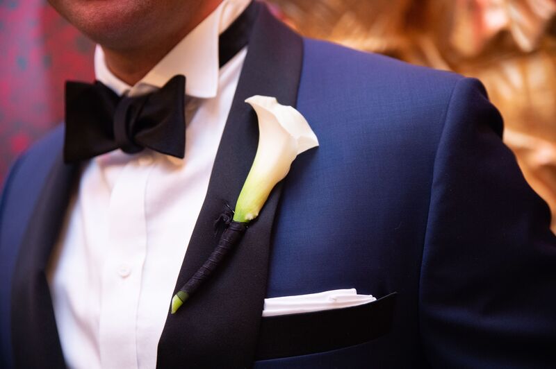 Groom in a blue tuxedo with black shawl collar and a white calla lily boutonniere