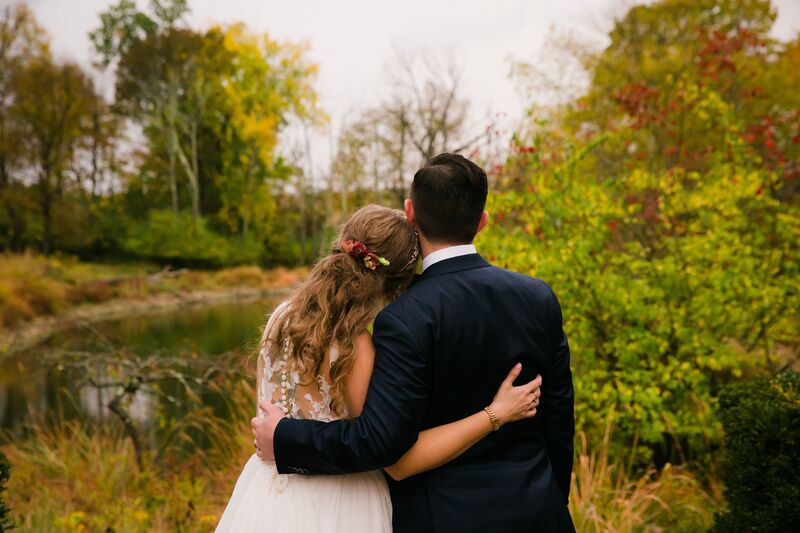 back view of the bride and groom looking over a pond a trees with fall colors