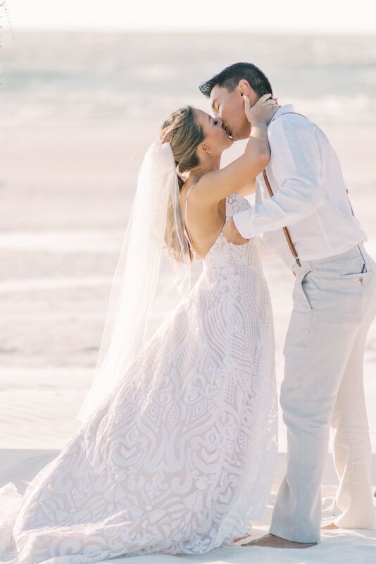 Just married! Newlywed couple kissing during their Sunset Beach Resort beach wedding