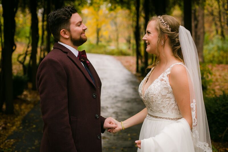 bride and groom holding hands while walking through the woods after a fall rain