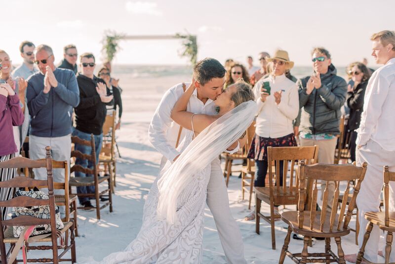 Wedding guests cheering as couple kiss after their Sunset Beach wedding