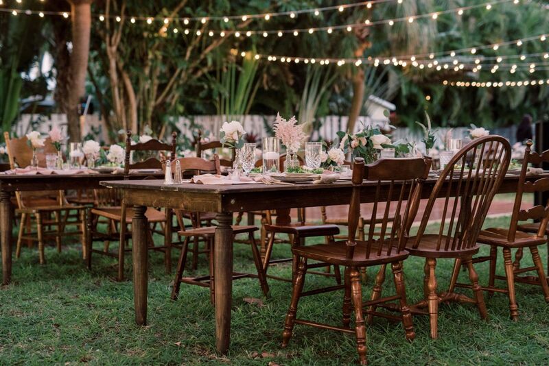 Outdoor wedding reception set with rustic wooden farmhouse tables and mismatched wooden dining chairs