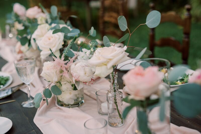 Pink table runner dotted with eclectic glassscontainers and pink and white flowers