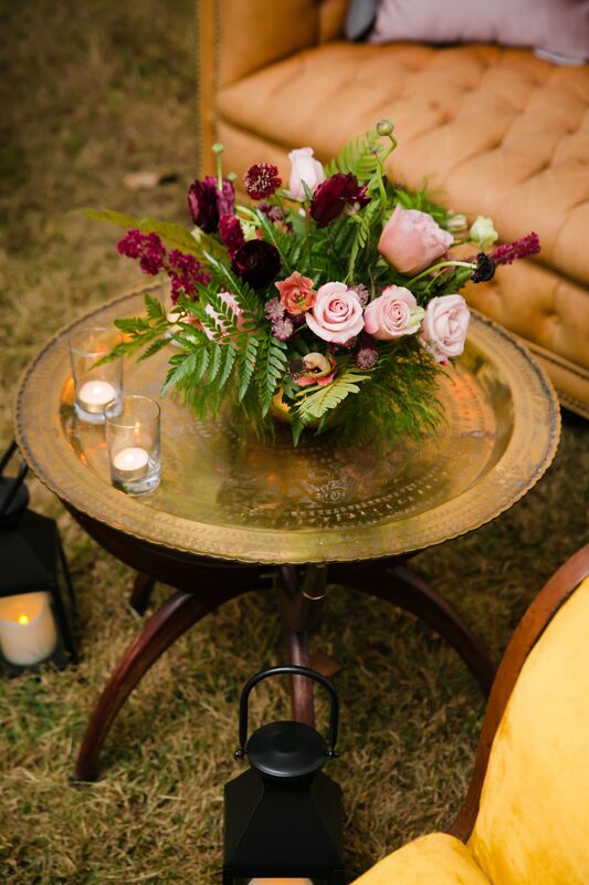 a pink and burgundy centerpiece on a vintage brass table surrounded by vintage lounge furniture