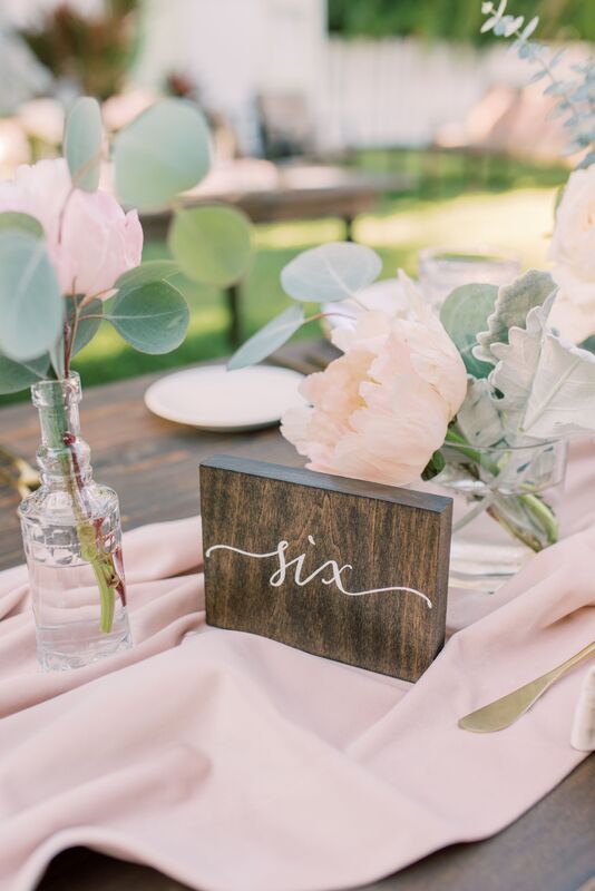 Rustic wooden table numbers paired with soft romantic pink florals and vintage glassware for an outdoor Siesta Key wedding