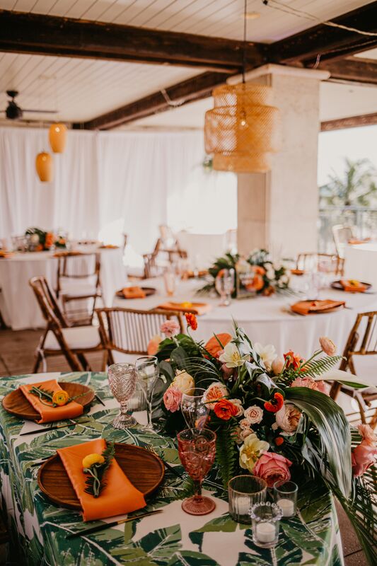 Tropical inspired wedding reception at the Ritz Carlton Beach Club with lush greenery, orange flowers and bamboo chairs