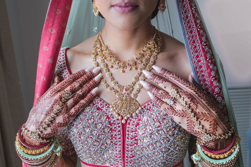 South Asian bride showing her hands covered with intricate henna designs, showcasing her bracelets and necklace