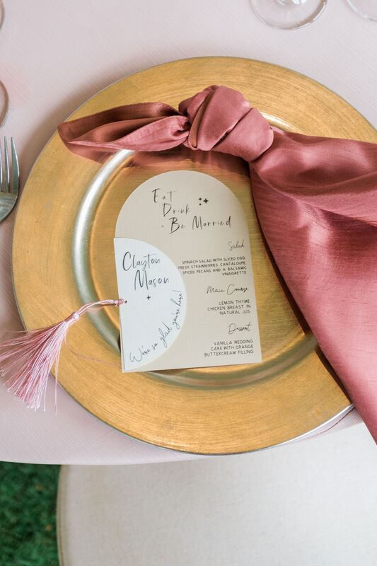 gold charge plate layered with custom menu card and knotted pink skin napkin