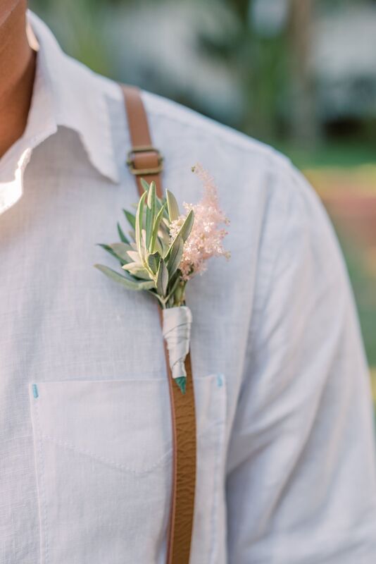 delicate wedding boutonniere of greenery and pink astilbe pinned to the grooms leather suspenders