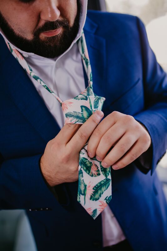 Groom in a blue suit putting on a tropical palm print necktie