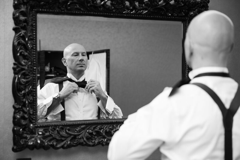 Groom looking in the mirror fixing is bow tie