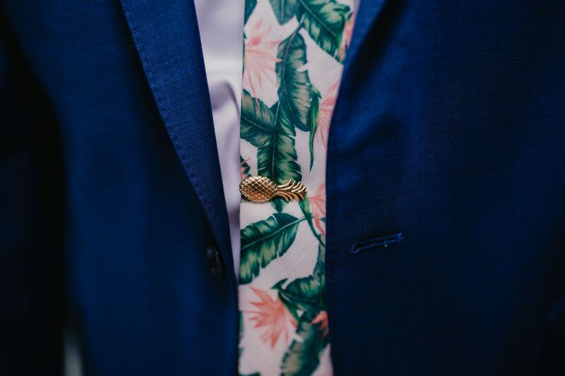 Groom wearing a blue suit and tropical necktie with gold palm tie clip
