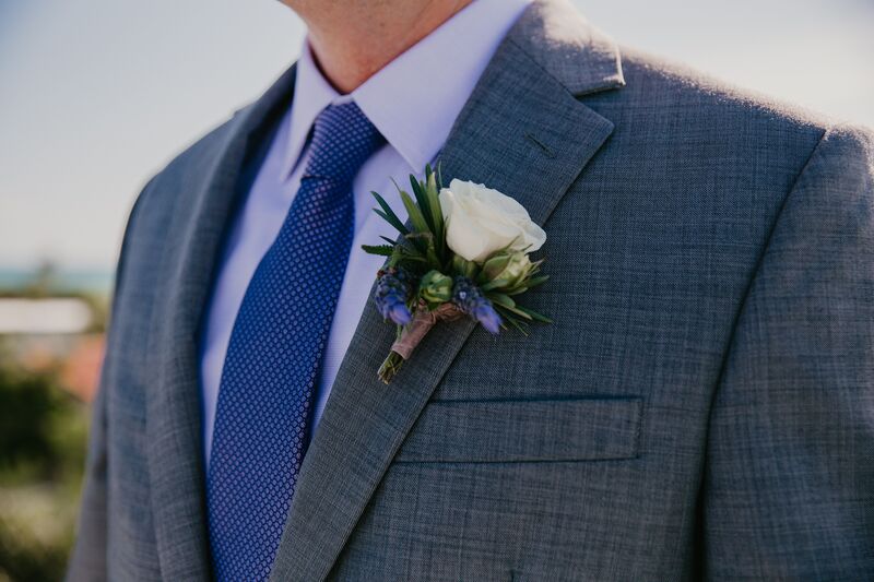 groom wearing a blue grey suit, blue tie and white boutonniere