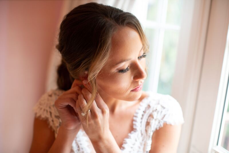 bride putting on earrings as she gets dressed for her wedding ceremony