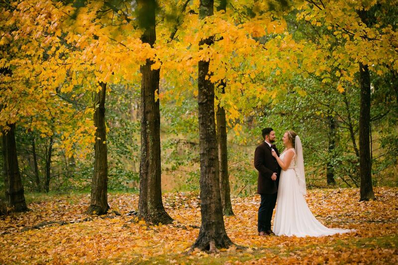 Bride and groom standing in the woods under trees with golden leaves