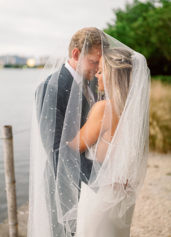 Waterside photo of bride and groom under her wedding veil