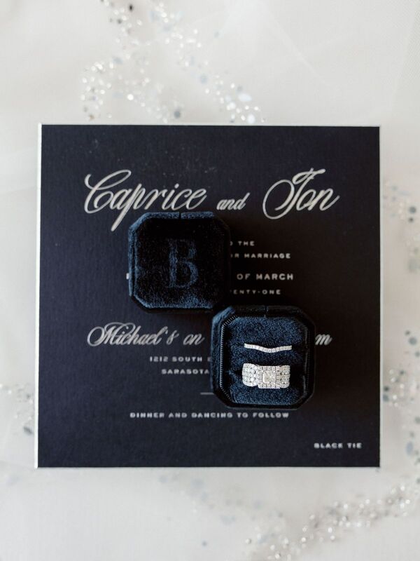 black wedding invitations as the background for the couple's wedding rings