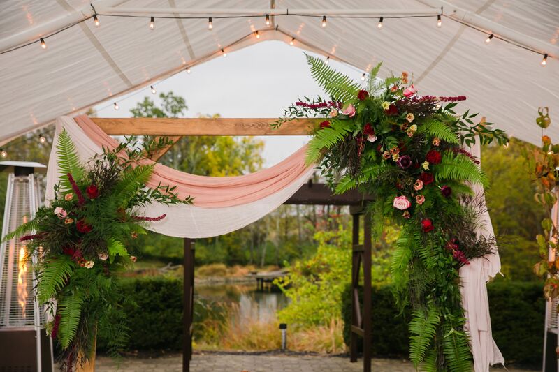 Wooden wedding arch swagger with pink and white fabric decorated with ferns and pink and burgundy flowers