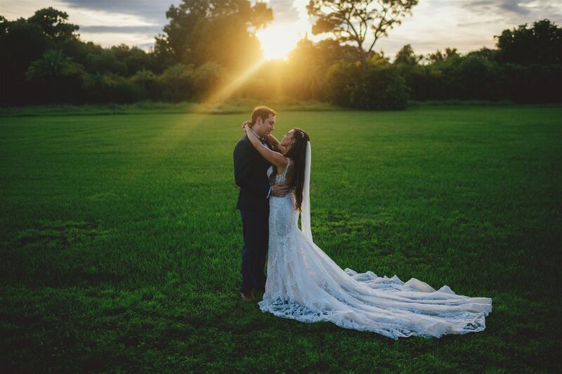 bride and groom in a field with the sun setting behind them