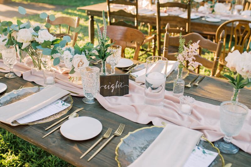 Outdoor wedding reception set with rustic wooden farmhouse tables and mismatched wooden dining chairs