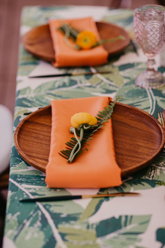 Tropical inspired wedding reception with modern wooden charger plates, orange napkins and a single orange flower