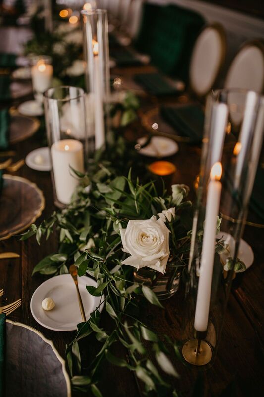 Wooden tables dressed in lush greenery, gold accents and white flowers