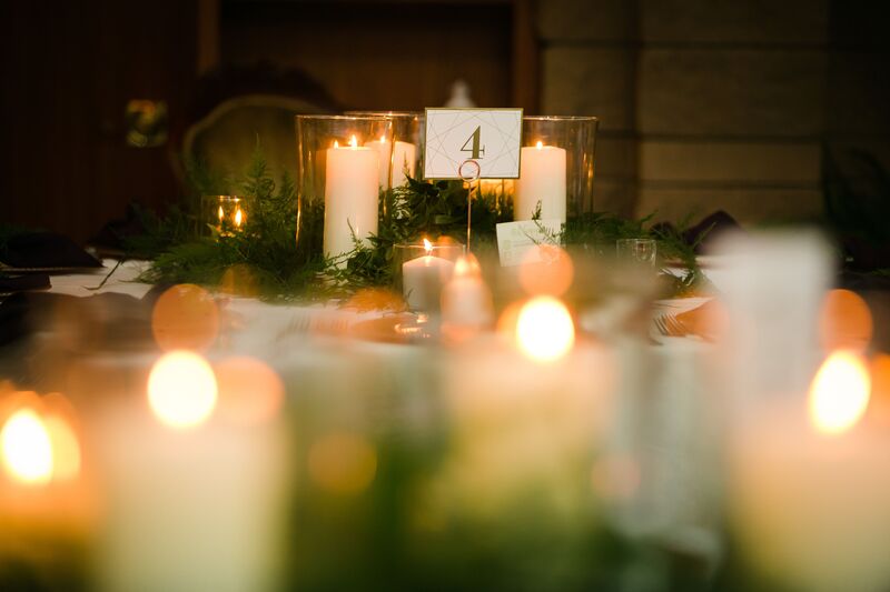 tables at a wedding reception decorated with pillar candles and ferns