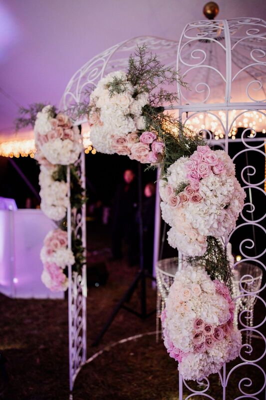 wrought iron gazebo covered with pink and white flowers to display a floating wedding cake