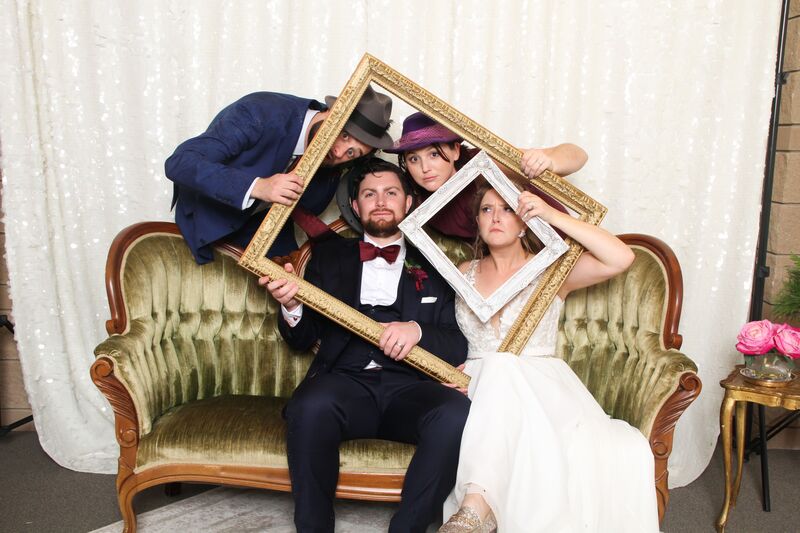 bride and groom posing for photos on a vintage sofa holding picture frames