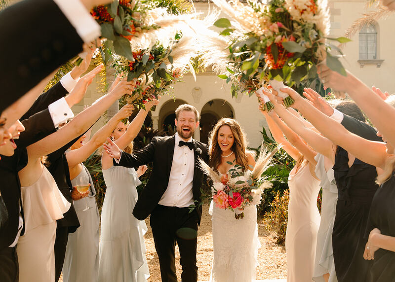 Bride and groom walking under an arch of flowers made by their wedding party