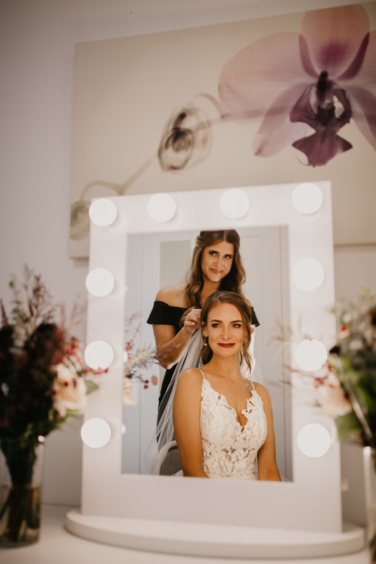bride looking into mirror as  her wedding veil is added to her hair