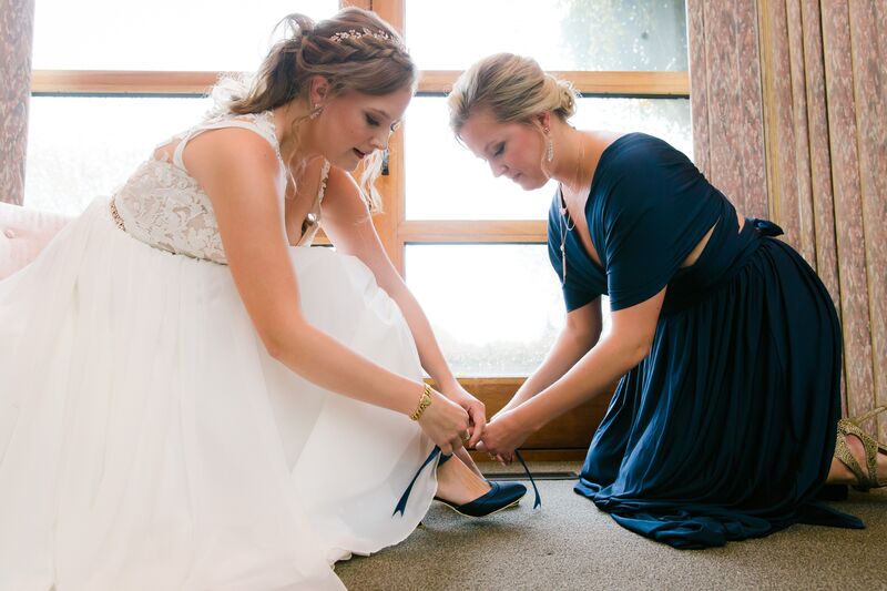 Maid of honor helping bride put on her blue wedding shoes