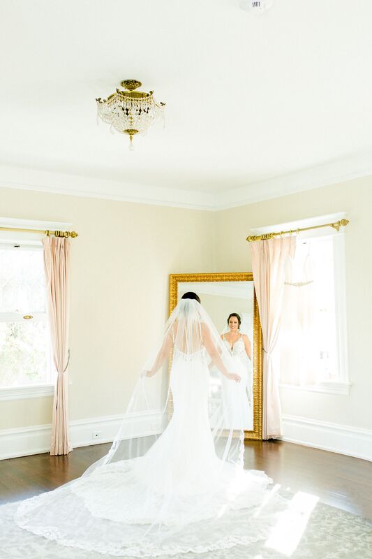 bride wearing a long flowing wedding gown and veil standing in front of a gold full length mirror