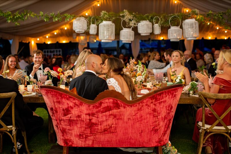 brie and groom sitting on a vintage red velvet love seat surrounded by Boho inspired wedding reception decor at Casa Ybel