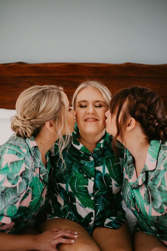 bridesmaids in tropical robes kissing bride on the cheeks