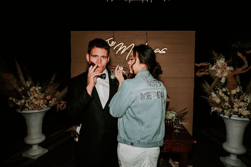 Bride in jean jacket smoking a cigar with her groom