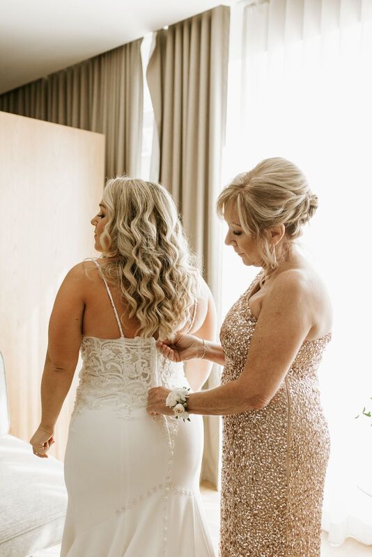 mother of the bride helping her daughter into her wedding gown
