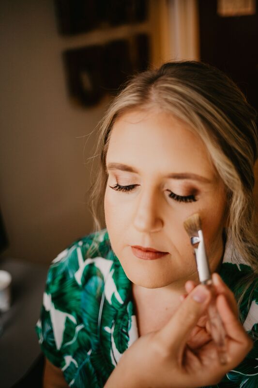 makeup artist applying blush to bride's cheeks