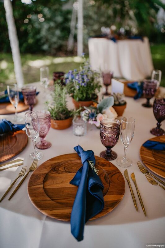 Place setting at a Sunset Beach Resort wedding reception. wooden charger plates, modern flatware and plants
